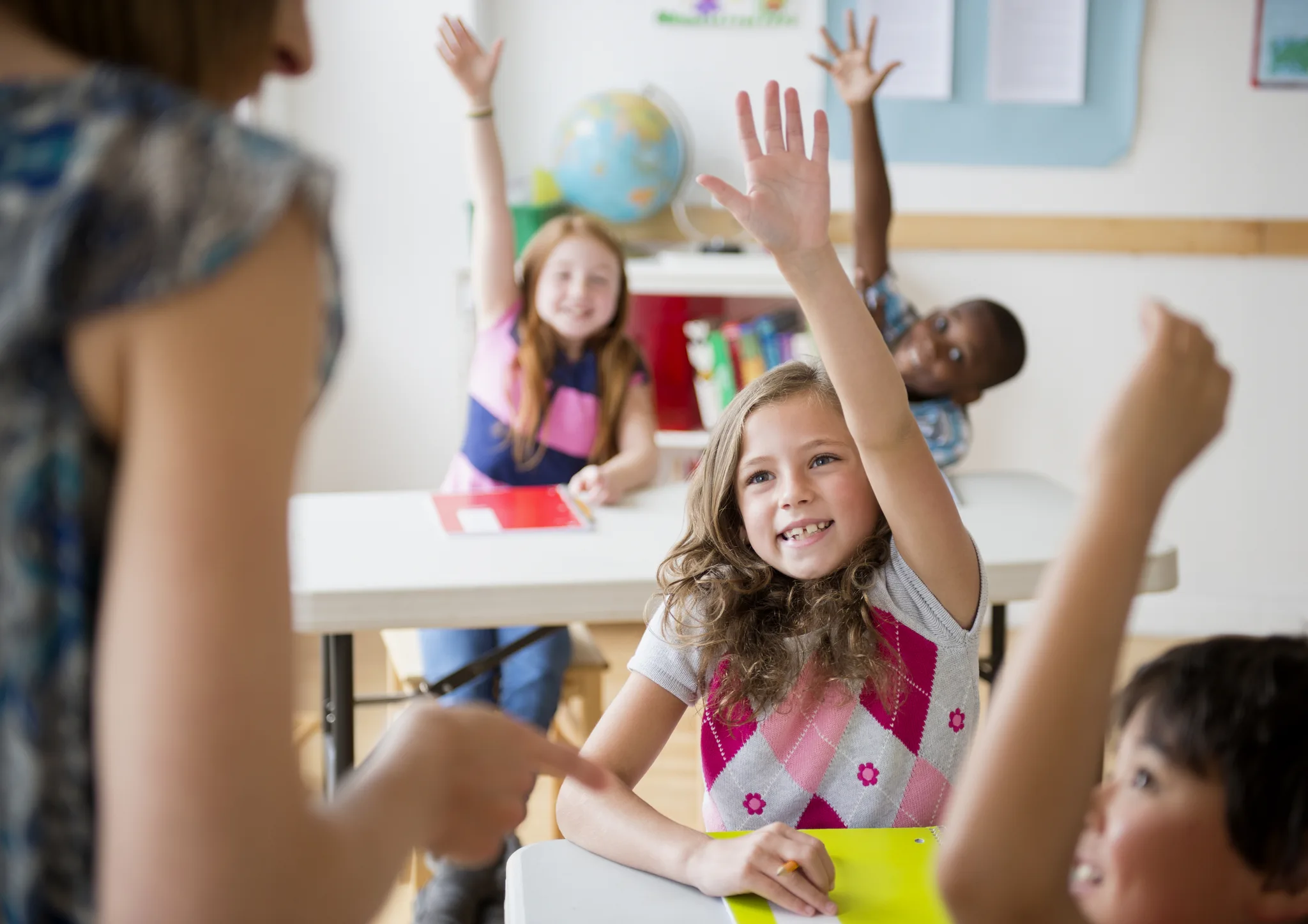 Elementary students raising their hands eagerly in a classroom