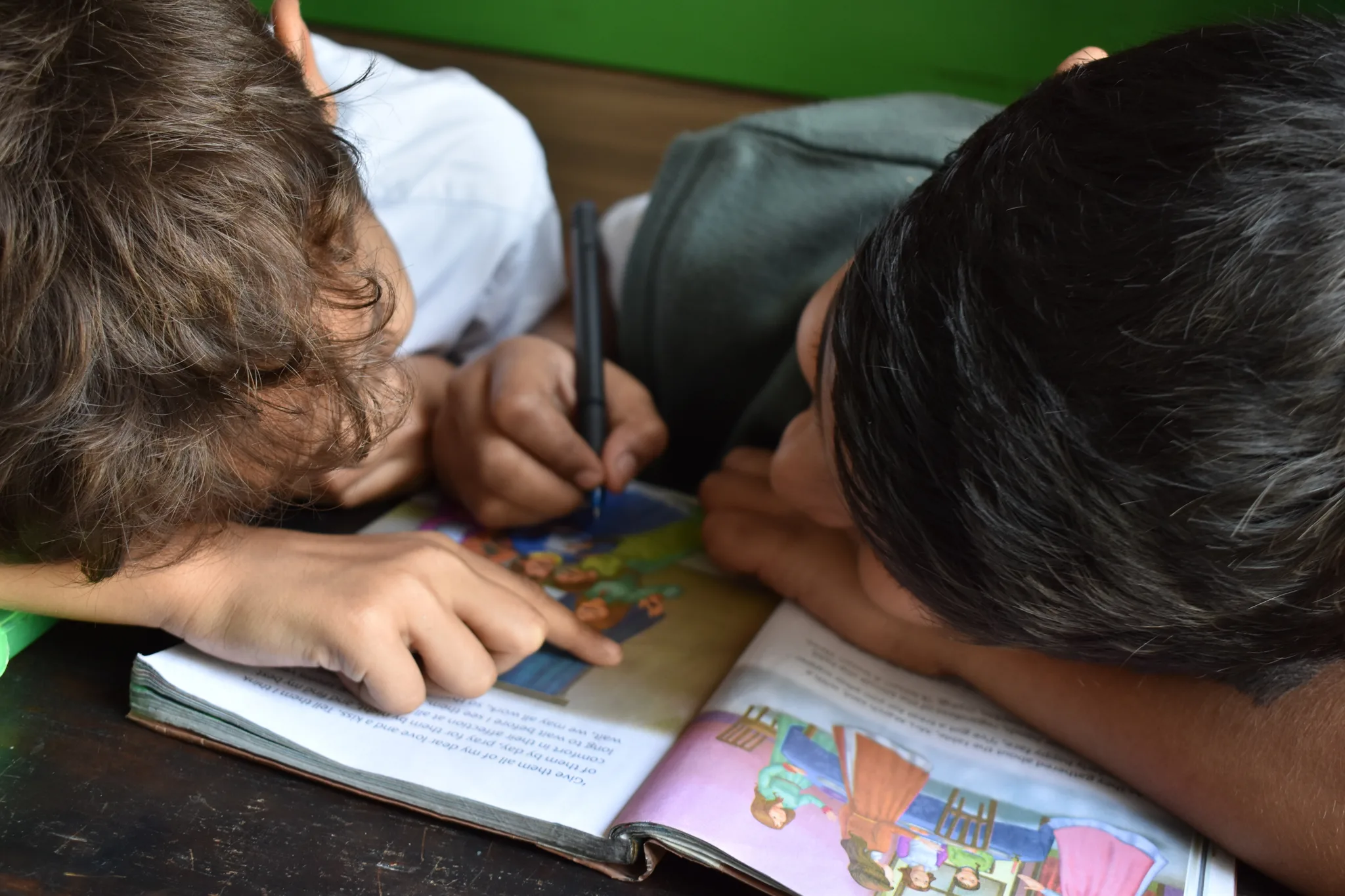 Two young boys lying on the floor reading and pointing at a colorful picture book